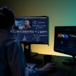 A woman engrossed in video editing on dual monitors in a dimly lit room.